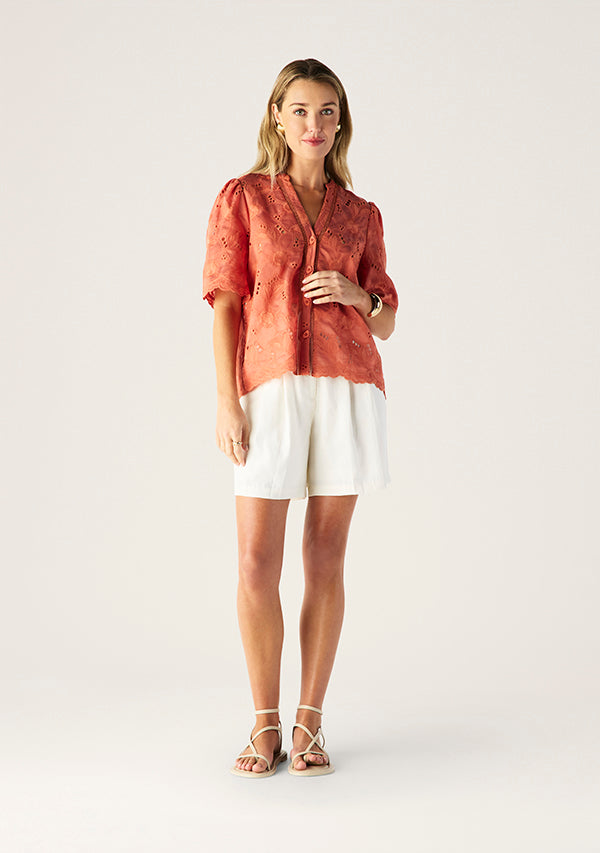 Woman wearing a coral blouse and white shorts on a light background