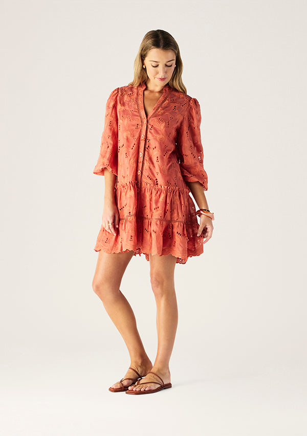 Woman wearing a coral dress with floral embroidery on a white background