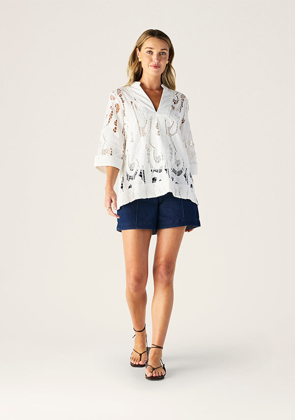 Woman wearing a white lace cover-up and navy shorts on a white background