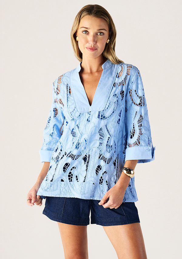 Woman wearing a light blue lace kimono-style top with navy shorts on a plain background