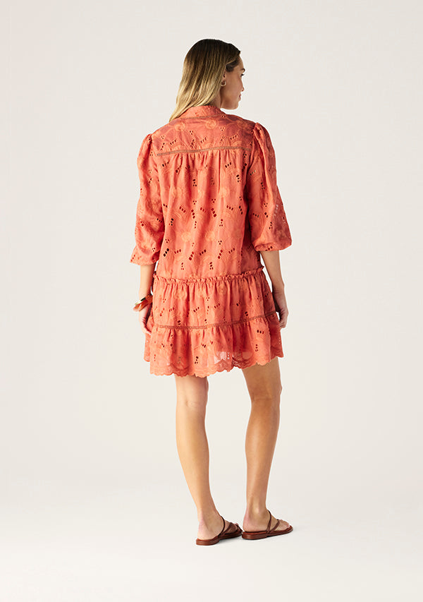 Woman wearing a coral dress with intricate detailing on a white background