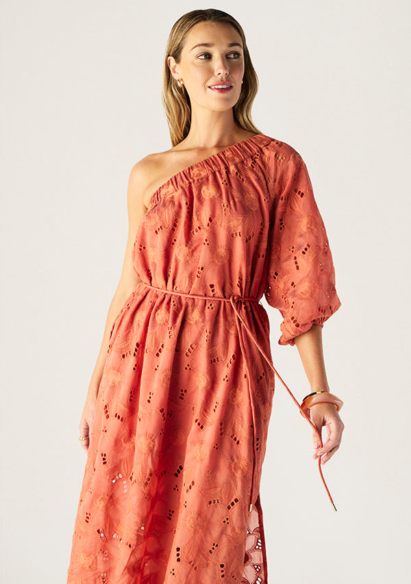 Woman wearing a one-shoulder pink dress with floral patterns on a plain background
